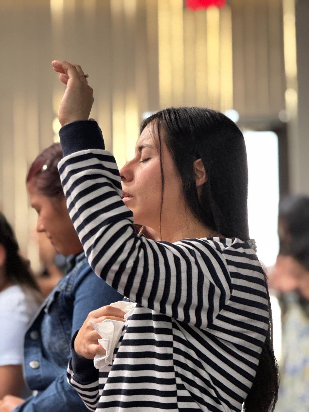 Una integrante de la congregación con la mano levantada durante la adoración